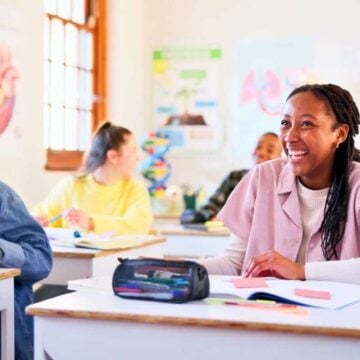 teen students in classroom smiling while working on financial literacy worksheets