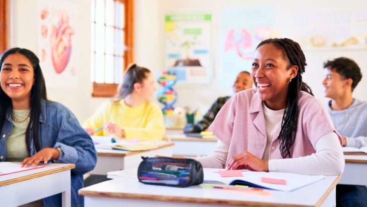 teen students in classroom smiling while working on financial literacy worksheets