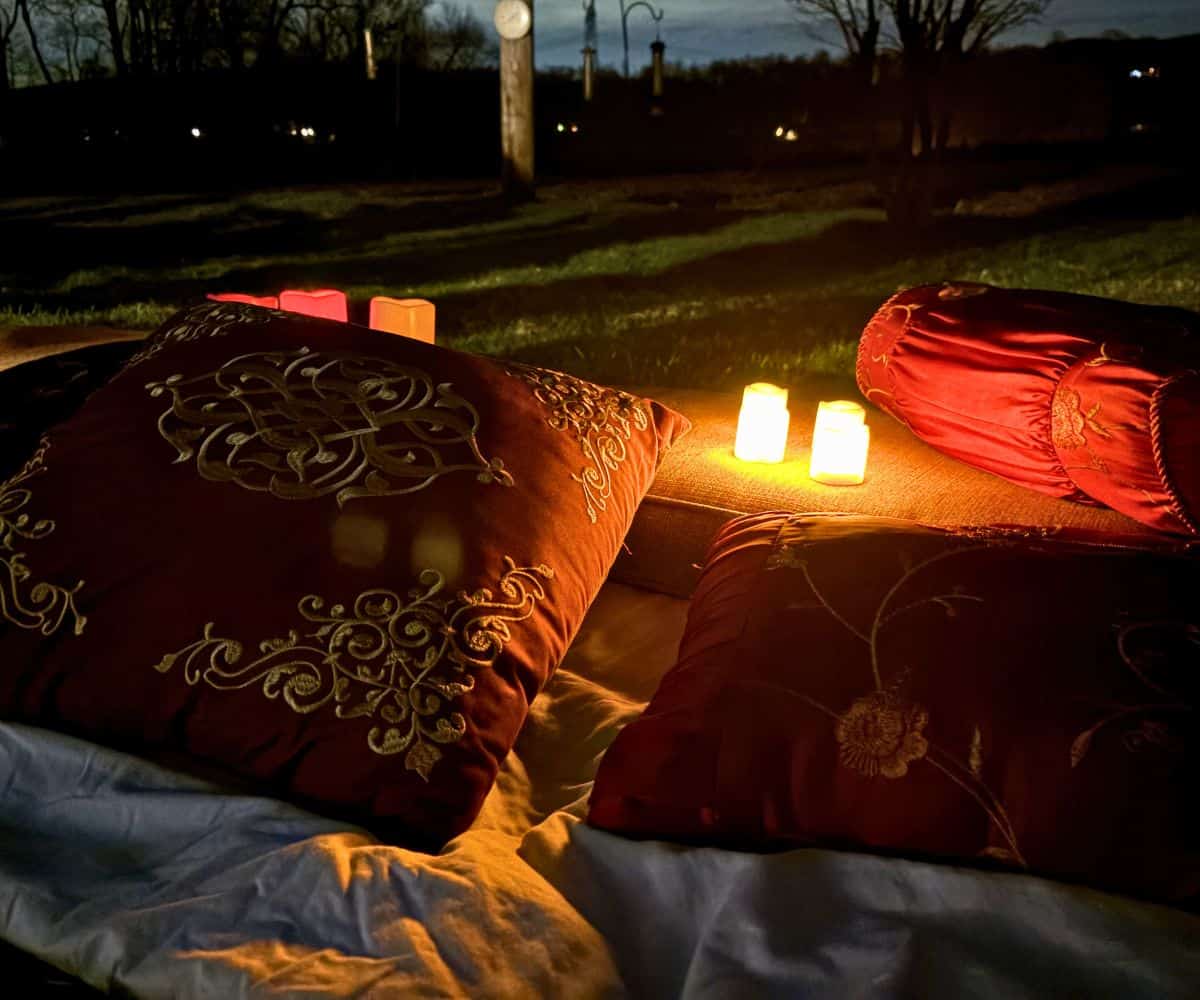 lots of large pillows and battery-operated candles on blankets in dark backyard