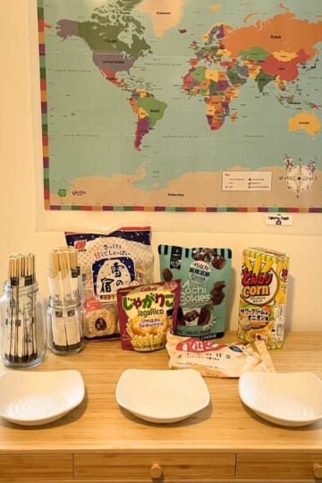 world map on wall, table filled with international snacks, chopsticks for everyone, and three bowls