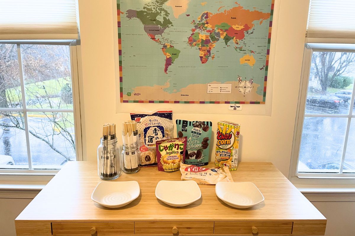 world map on wall, table filled with international snacks, chopsticks for everyone, and three bowls