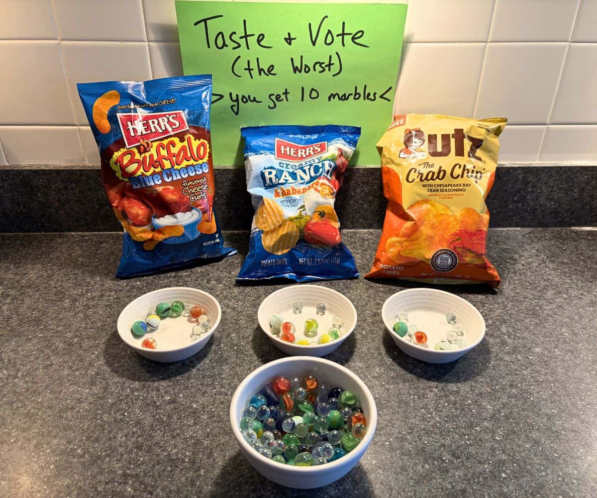 Three bags of chips with three bowls in front of them, and sign "taste and vote the worst - you get 10 marbles" with bowl of marbles
