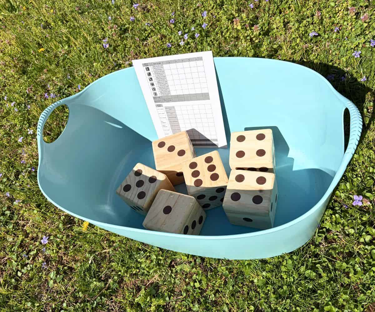 big teal basket filled with giant yard dice and a scoring card out on grass
