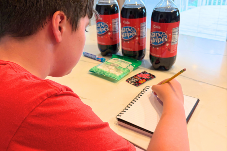 child making prediction in notebook in front of 3 2-liters of off-brand cokes and some candies