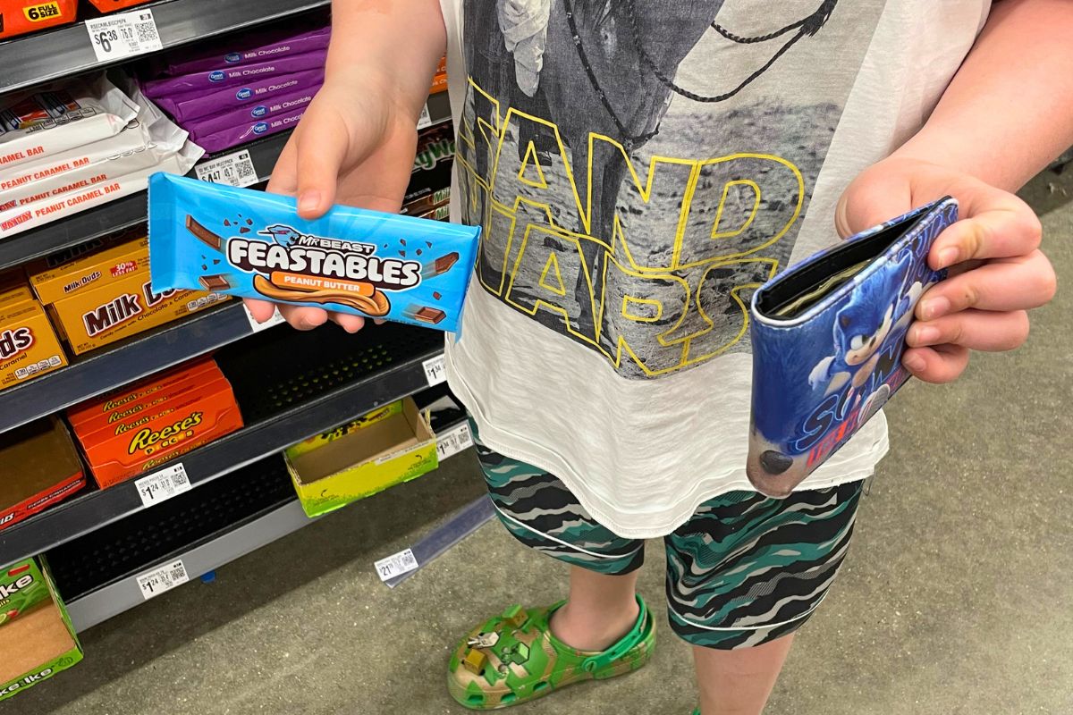 boy with wallet in one hand and Feastables in the other to buy