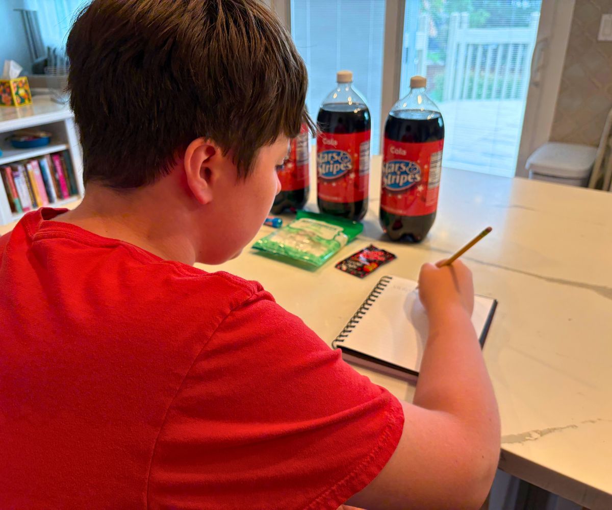 boy making prediction about exploding candy trials in front of three 2-liter bottles of off-brand cokes and various candies