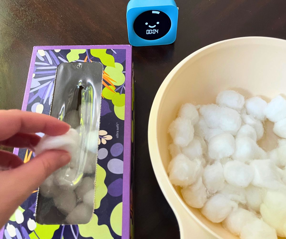 bowl with cotton balls, timer, and person stuffing cotton bals into empty tissue box